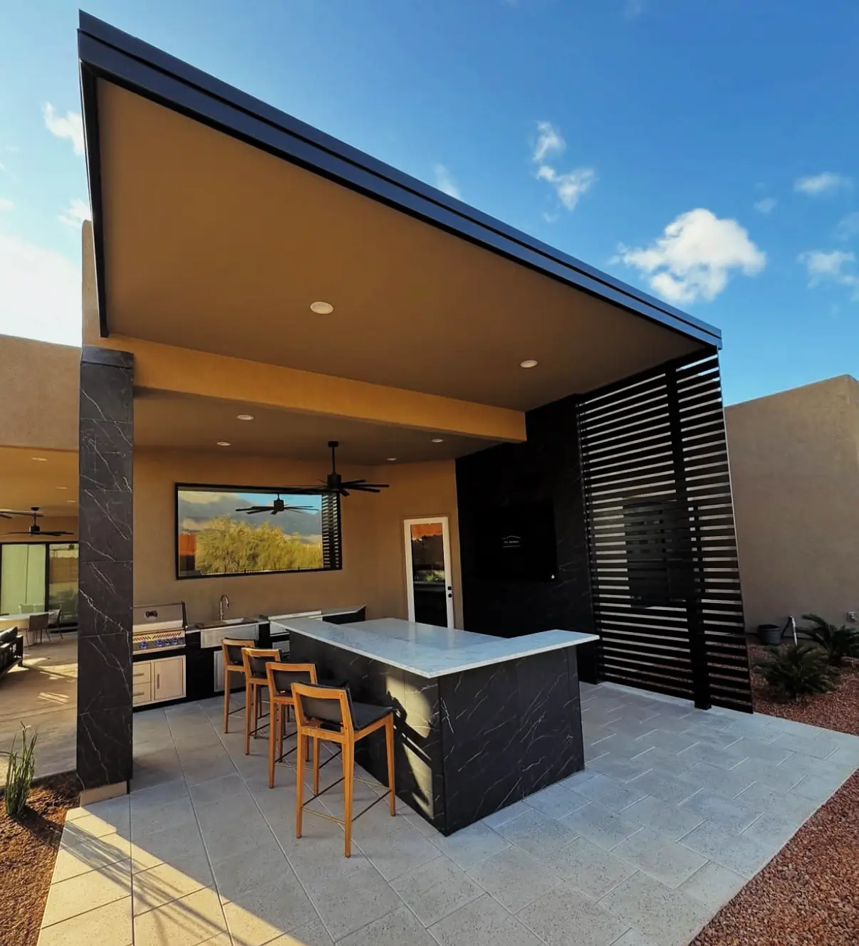Outdoor kitchen island with bar seating and a mounted TV under a modern covered patio