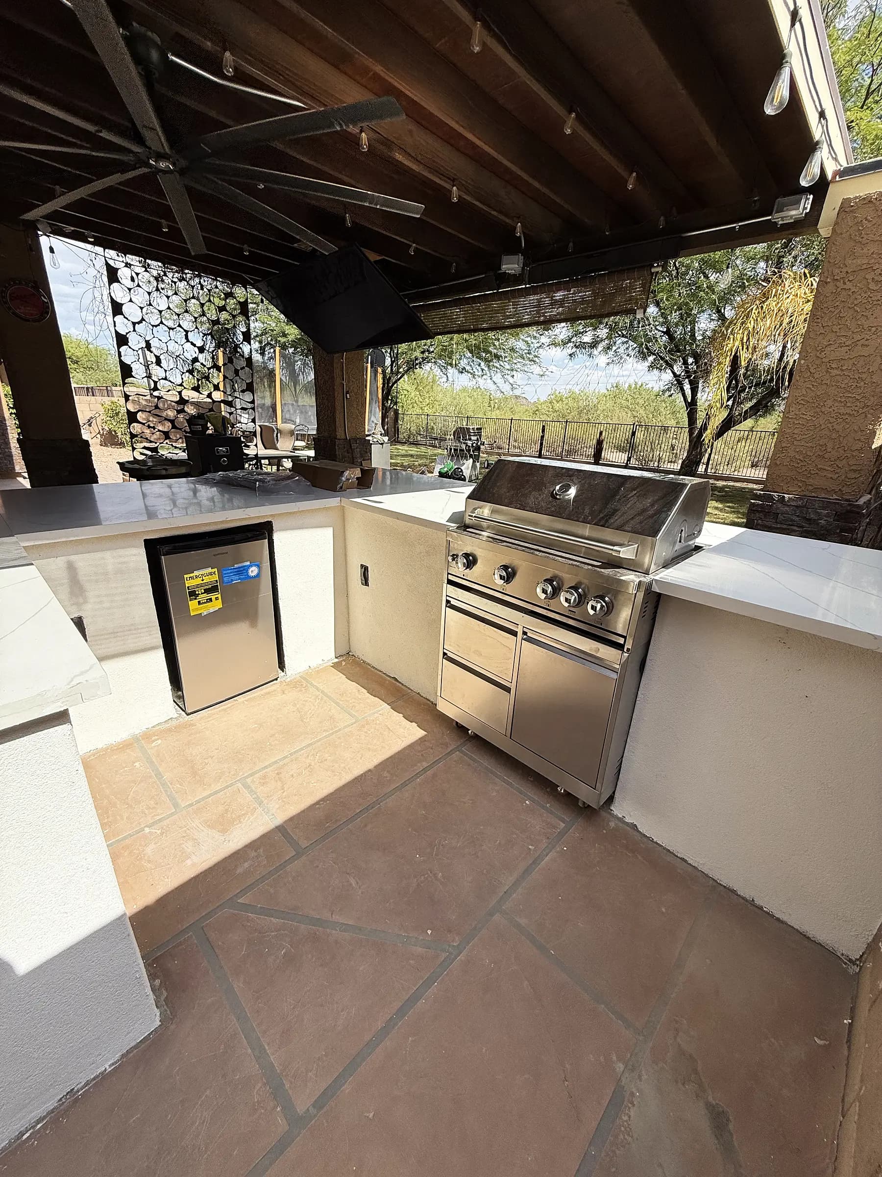 Built-in grill and stainless fridge in an L-shaped outdoor kitchen with a stone feature wall behind