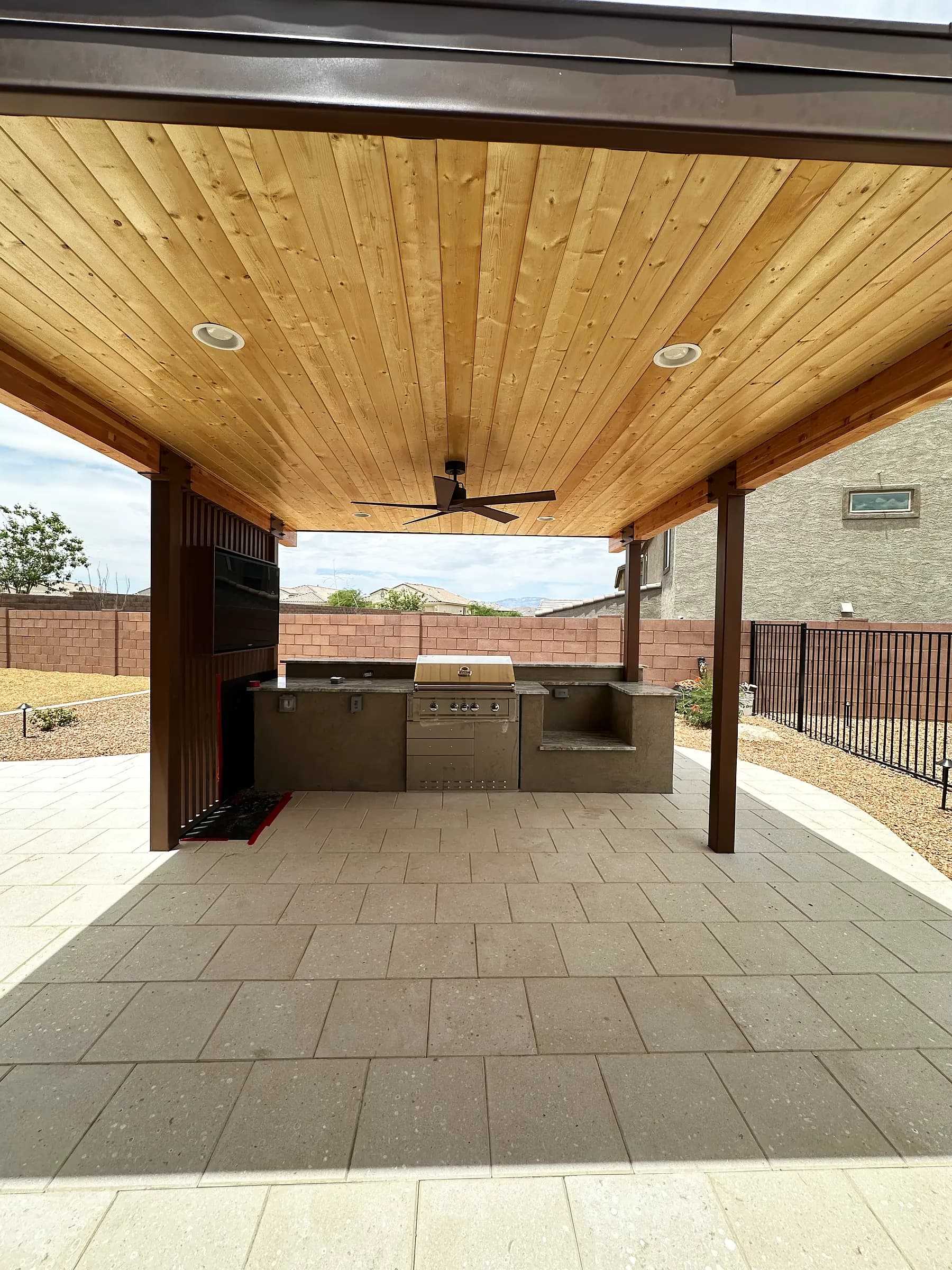 Finished outdoor kitchen with a built-in grill under a wood-ceilinged ramada, on a large-format paver deck in Tucson