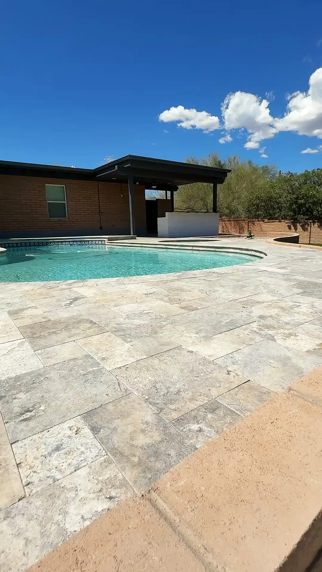 Finished Tucson backyard by AYJ Construction: silver travertine pool deck, brick home with a covered deck, and an artificial turf lawn