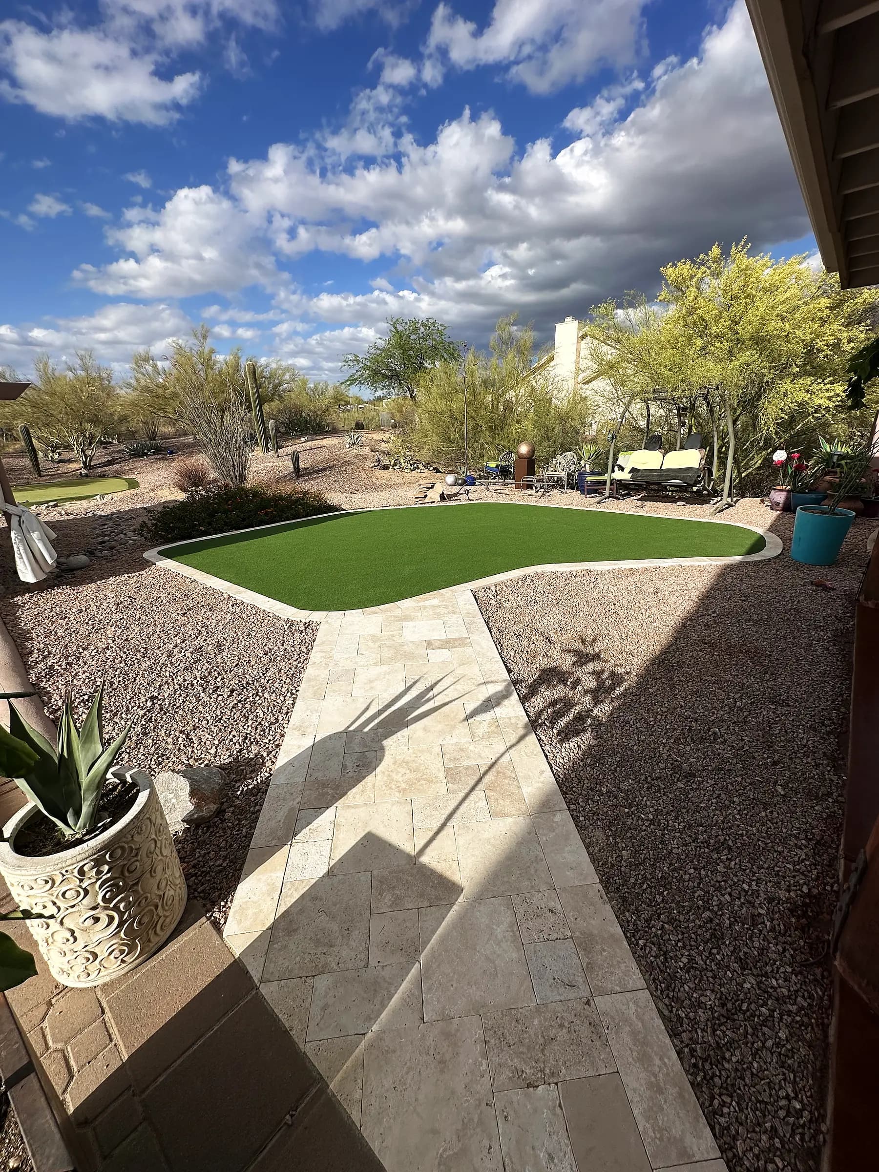 Travertine walkway curving past a custom-shaped artificial turf lawn on a Sonoran desert lot