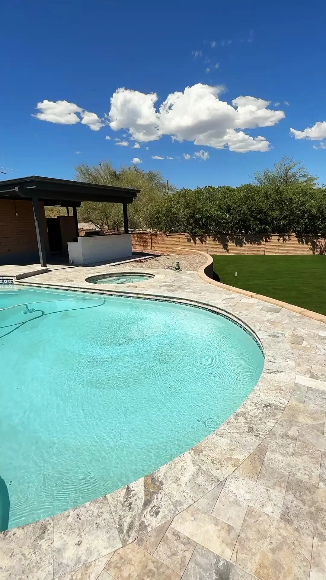 Travertine coping meeting an artificial turf lawn at the edge of a Tucson pool