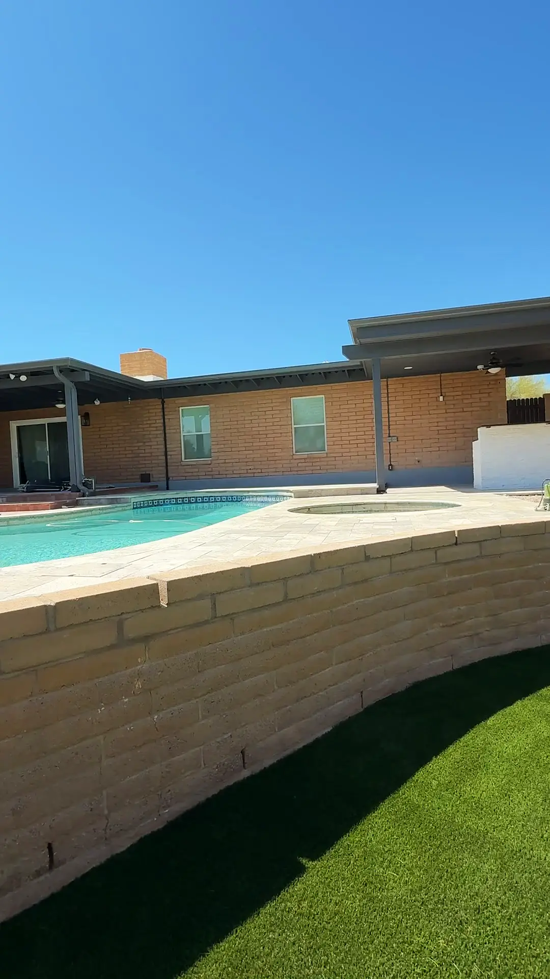 Curved split-face seat wall separating the raised turf lawn from the travertine pool deck