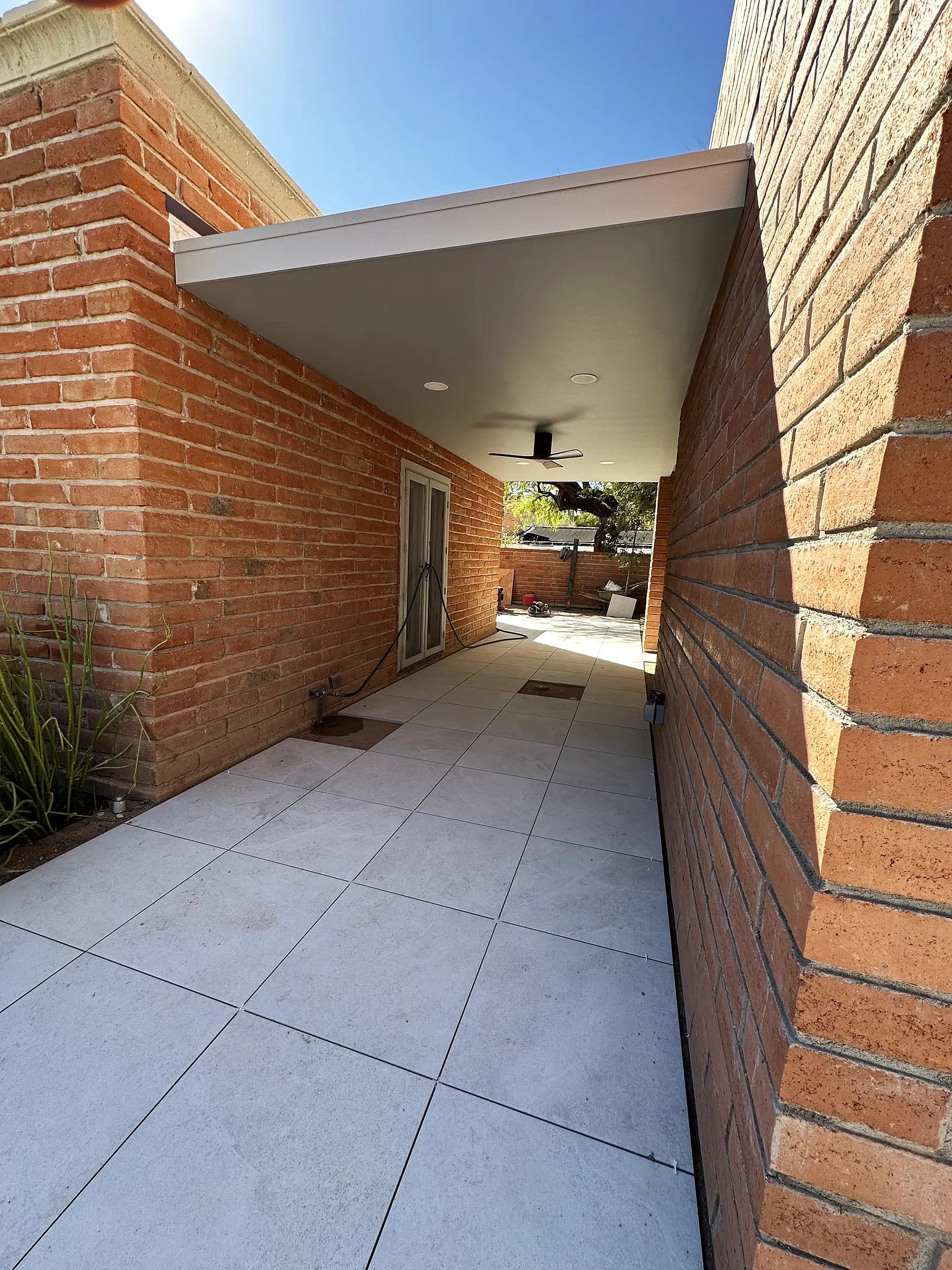 Porcelain walkway leading toward a shaded courtyard on a Tucson brick home