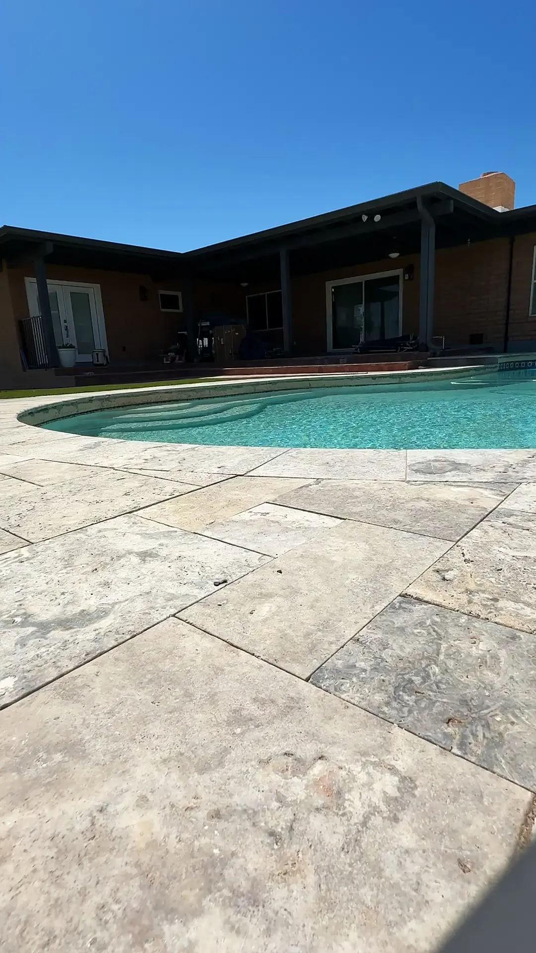Wide view of a French-pattern silver travertine pool deck in full Tucson sun