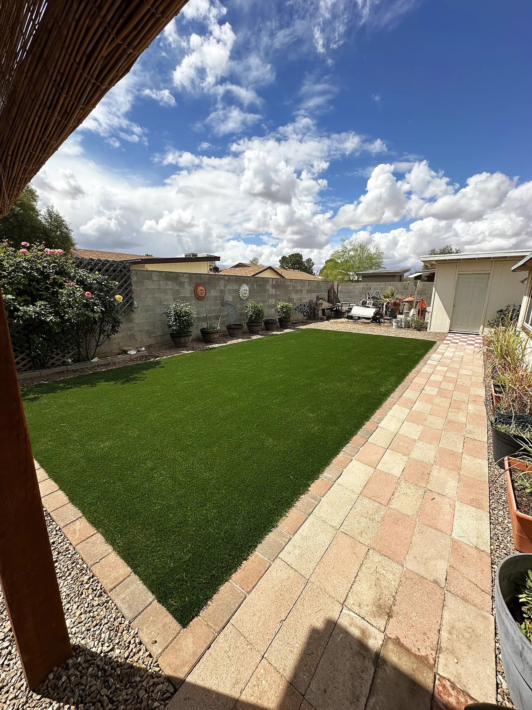 Paver walkway running alongside an artificial turf lawn under a block perimeter wall